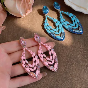 Elegant pink and blue rhinestone cutout drop earrings displayed on a hand and wooden table.