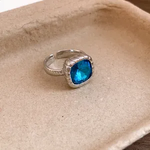 Dettaglio di un anello in argento regolabile con una gemma quadrata blu vibrante.