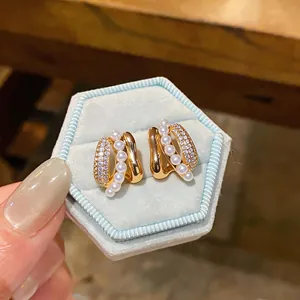 Close-up of C-shaped gold stud earrings with pearls and zirconia in a blue box