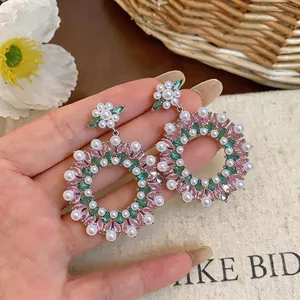 Vintage oversized hoop earrings with pink and green zircon and pearls on hand.