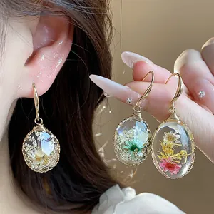 Close-up of resin water drop earrings with real dried flowers and gold hooks