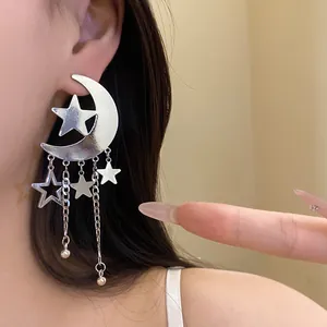 Macro detail showing elegant silver crescent moon and dangling star tassel earrings.