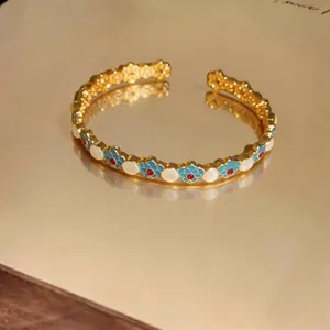 Vista macro dettagliata del bracciale rigido dorato con fiori in smalto blu