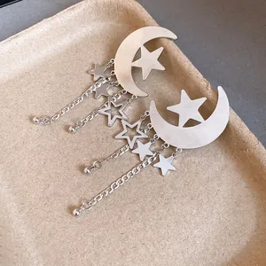 Close-up of silver-tone crescent moon and star earrings with dangling tassels.