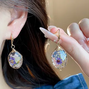 Macro detail shot of teardrop resin earrings featuring embedded real purple dried flowers