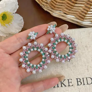 Close-up detail of vintage hoop drop earrings with pink zircons and white pearls held in hand