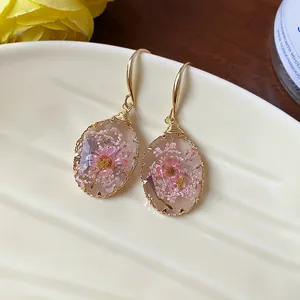Close-up of elegant resin teardrop earrings with pink dried flowers and gold hooks.