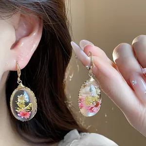 Close-up of teardrop resin earrings with dried flowers on model's ear