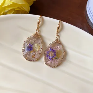 Detail shot of teardrop resin earrings featuring delicate real dried flowers inside.