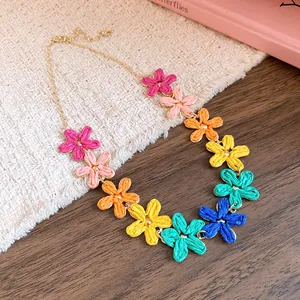 Close-up detail of bohemian colorful woven raffia flower necklace with elegant gold-tone chain