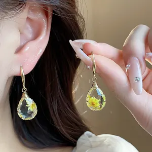 Close-up of resin teardrop drop earrings with delicate yellow dried flower detail