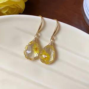 Close-up of teardrop resin earrings featuring delicate yellow dried flowers inside.