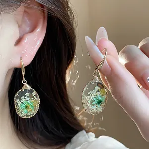 Close-up of resin teardrop earrings with preserved green flowers and gold-tone hooks