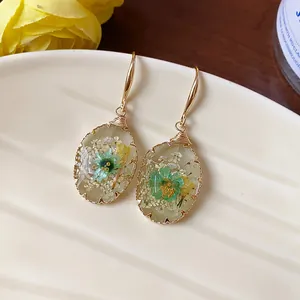 Detailed close-up of resin drop earrings with embedded green dried flowers