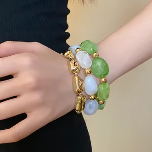 Close-up detail of layered irregular acrylic stone bracelets in green, white, and gold finish