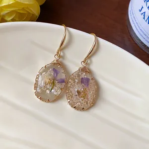 Detailed view of handmade resin drop earrings with embedded purple and white dried flowers.
