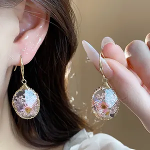 Close-up of elegant waterdrop resin earrings with pink dried flowers and gold hooks.