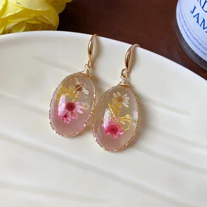 Close-up of elegant oval resin earrings with embedded pink and white dried flowers