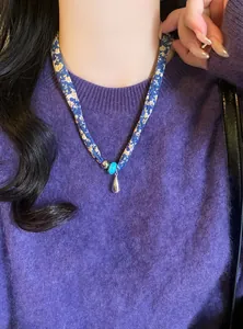 Primo piano di una collana a foulard in seta a fiori blu con un ciondolo a goccia in argento