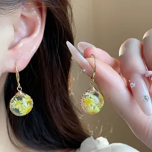 Exquisite detail of handmade resin earrings with embedded yellow dried flowers in gold wire