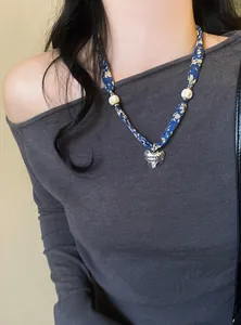 Primo piano di una collana sciarpa in seta floreale blu con ciondolo a cuore argento