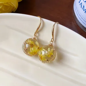 Close-up of resin sphere earrings with yellow dried flowers and gold hooks