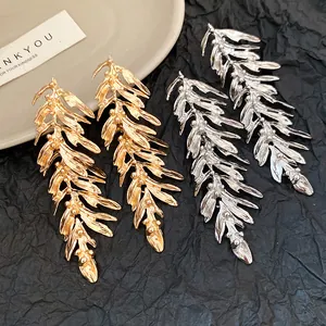 Detail shot of textured gold and silver leaf feather tassel earrings on dark backdrop