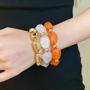 Stacked irregular acrylic stretch bracelets in gold, white marble, and vibrant orange