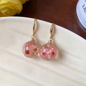 Macro view of gold drop earrings with pink dried flowers in clear resin spheres
