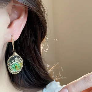 Detail of resin teardrop earrings with embedded green and white dried flowers and gold hooks.