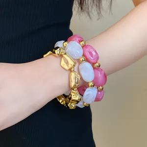 Detail of irregular geometric gold and marble acrylic elastic bracelets on wrist.