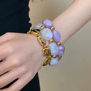 Detail view of irregular geometric acrylic and gold-toned elastic bracelets on wrist.
