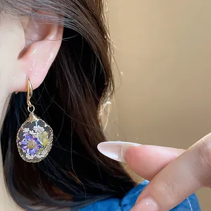 Close-up detail of a handmade teardrop resin earring with embedded dried purple flowers