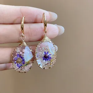 Detailed macro shot of handmade resin waterdrop earrings with dried purple flowers and gold hooks
