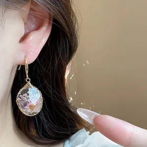 Close-up of resin teardrop earrings with pink dried flowers design