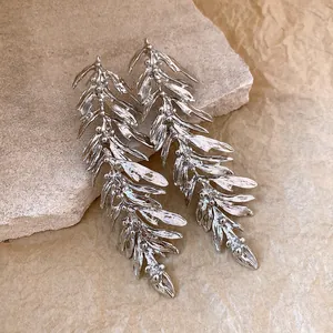 Macro detail view of elegant silver leaf branch drop earrings on a textured stone background