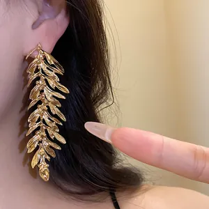 Close-up view of a large golden leaf branch earring worn on an ear, showing metallic texture.