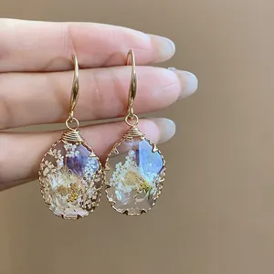 Close-up of handmade resin teardrop earrings with embedded purple and white dried flowers