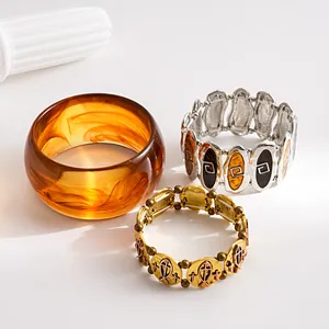 Close-up detail of amber resin bangle and vintage metallic fish cross charm bracelets.
