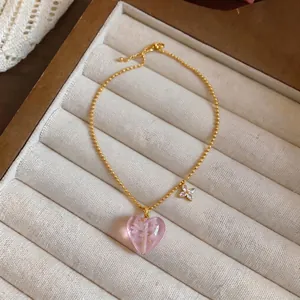 Gentle pink heart-shaped glass pendant necklace with gold beads on beige jewelry tray