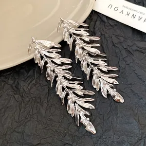 Close-up of silver-toned leaf earrings with detailed feather tassel on black paper.