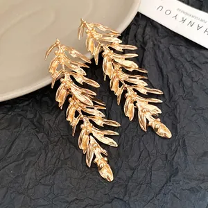 Detailed view of elegant gold leaf feather tassel earrings on textured black paper.