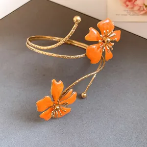 Detail view of an elegant gold armlet featuring two vibrant orange enamel flowers.