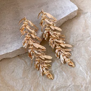 Macro detail view of elegant golden leaf feather tassel earrings on stone slab