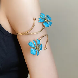 Detailed view of an elegant gold-toned armlet with blue enameled flower accents on model's arm