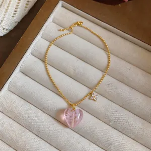 Detailed view of pink heart glass pendant necklace on beige velvet display tray.