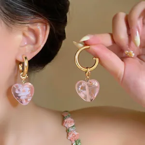 Exquisite pink heart-shaped glass earrings with gold hoops shown on ear and hand detail