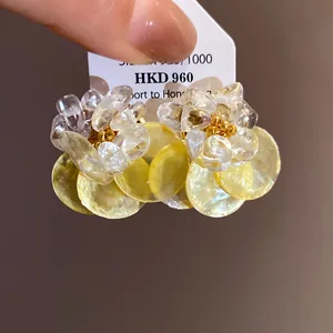 Macro detail of summer stud earrings with clear crushed stones and yellow shell discs.