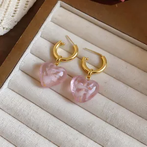 Close-up of pink marbled heart pendants on gold hoop earrings in a display tray