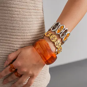 Close-up of amber resin bangle and vintage gold fish charm bracelet on model's wrist.